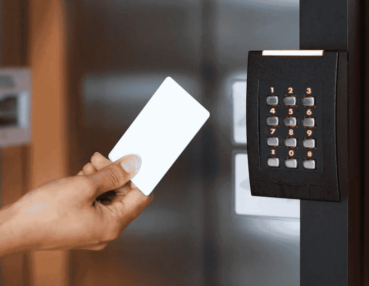 Door access security panel with number pad buttons and a proximity access card held in front of the panel by the hand of a person.